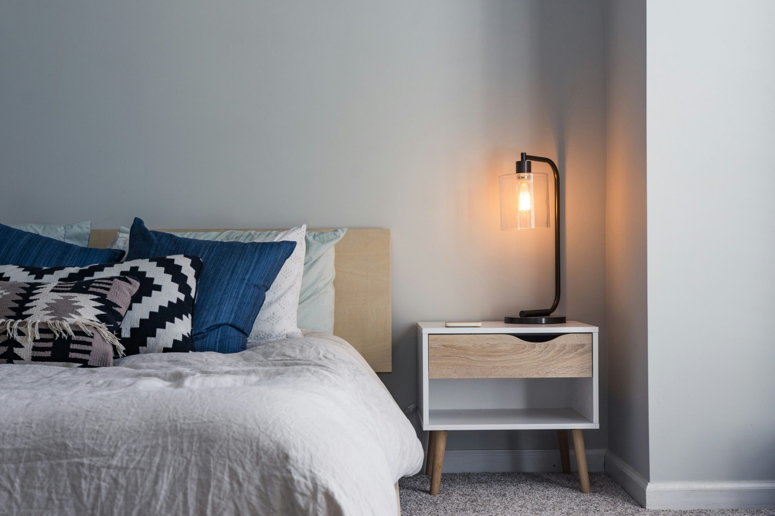 lit avec parure claire plus des coussins graphiques et d'autres bleus, avec un chevet et une lampr design noire