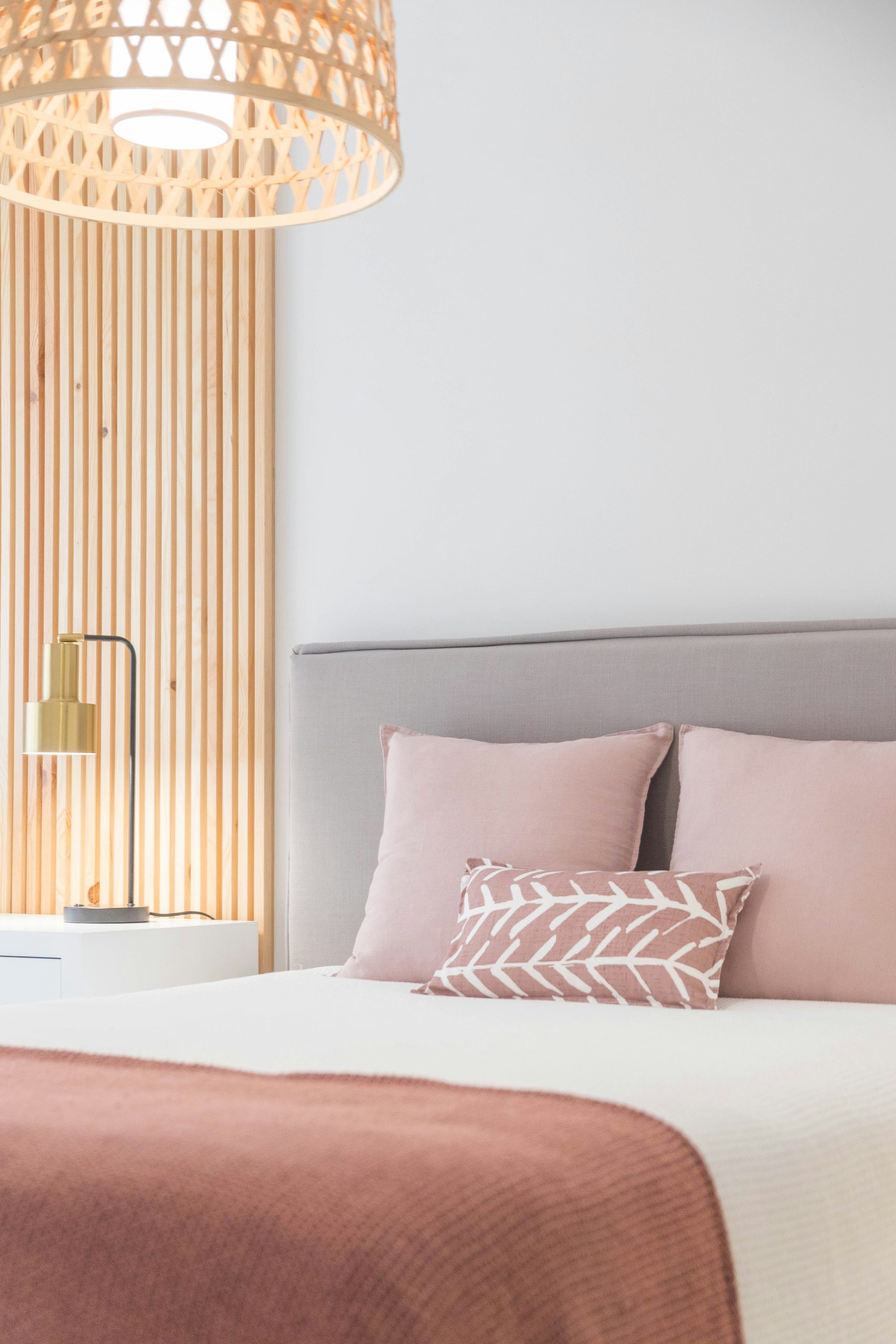 coussin et couette rose sur un lit gris avec mur panneau bois